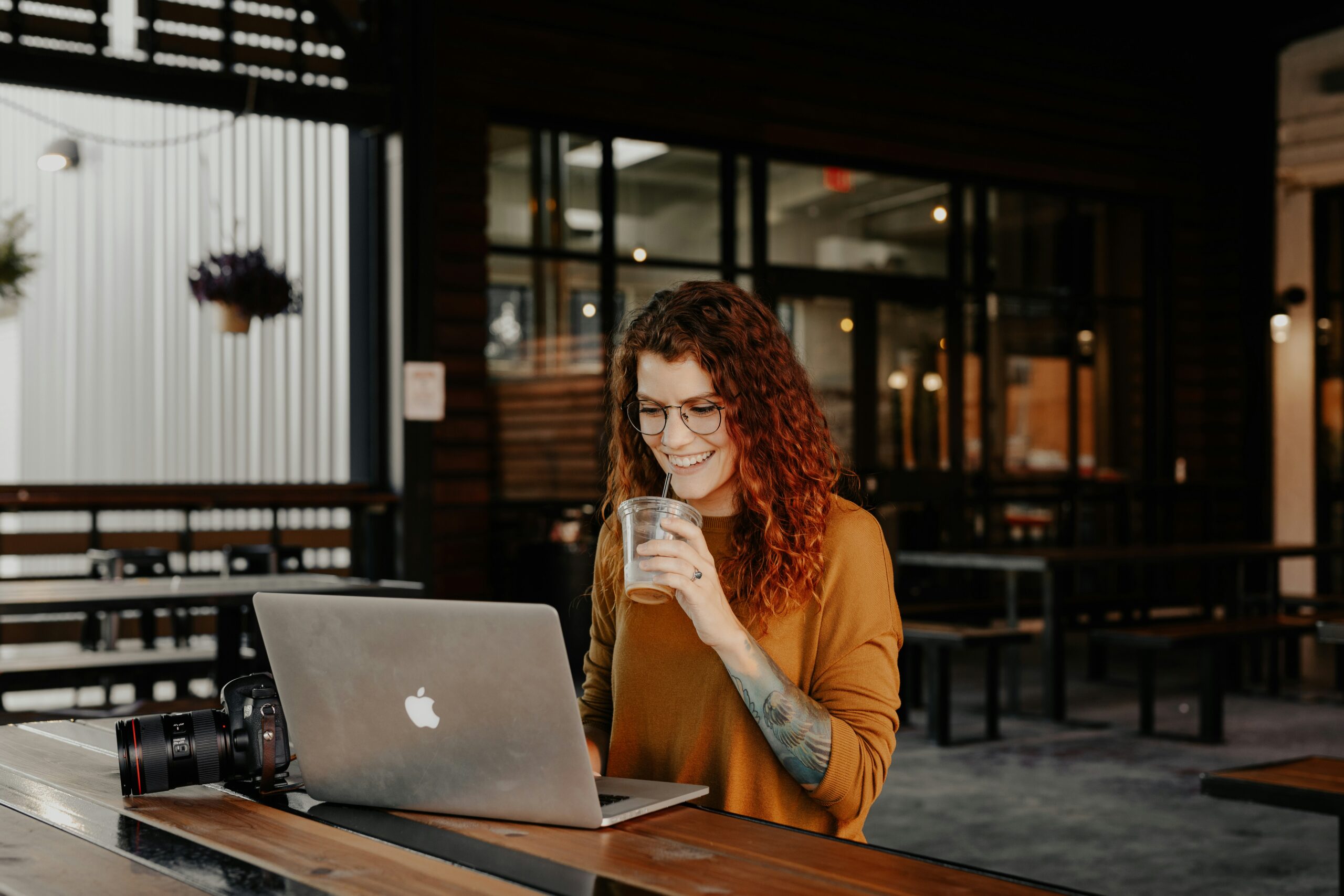 A photographer on her computer, smiling while she's about to take a sip of her coffee.